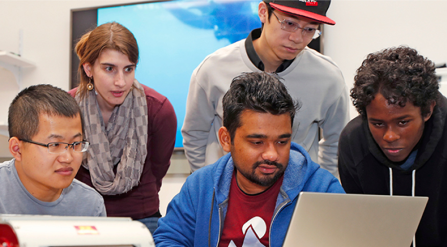 group of diverse students crowded around a laptop working together